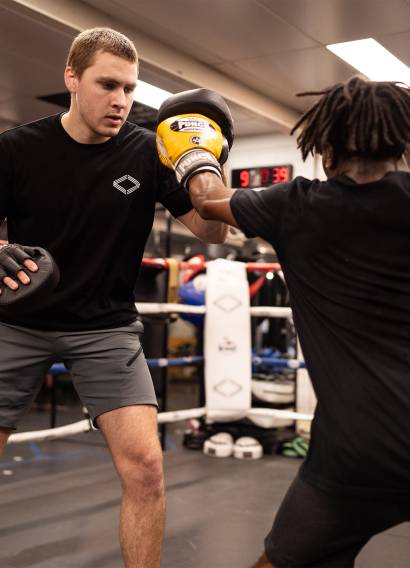Trainer demonstrating boxing technique with a student in the ring.